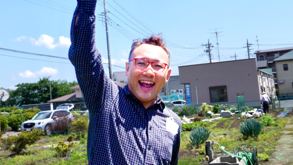 中川さんの青空の下で左手を上に挙げてはつらつとした表情